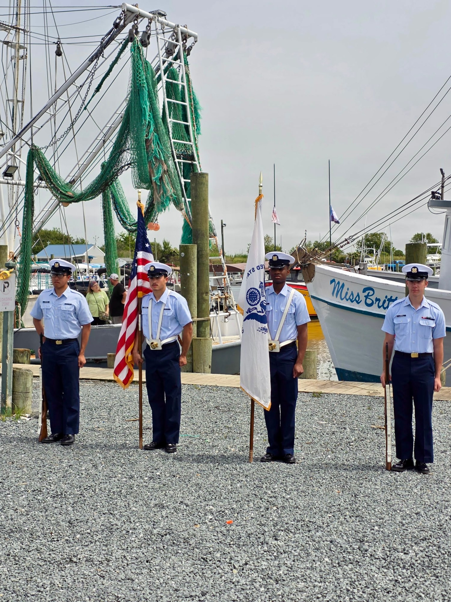 Four uniformed men stand with flags near boats in a harbor.