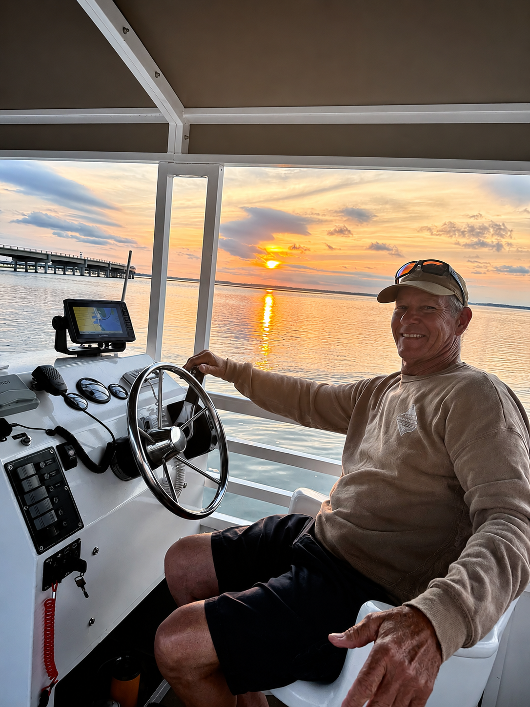 Man steering a boat at sunset on a calm body of water.